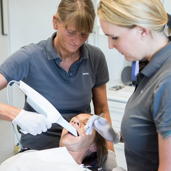 En tandlaege og en klinikassistent som er i gang med at behandle en patient i tandlaegestolen